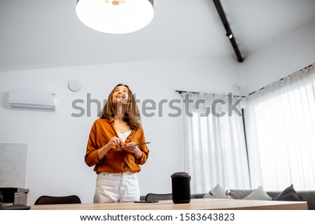 Young woman controlling home light with asmart home in the living room. Concept of a smart home and light control with mobile devices