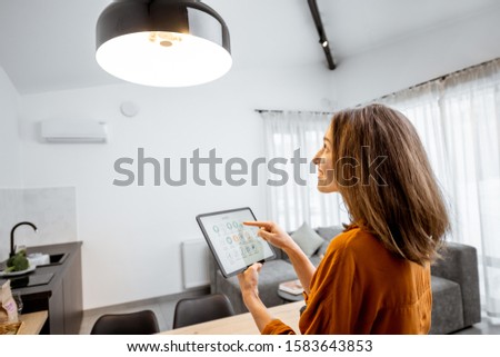 Young woman controlling home light with a digital tablet in the living room. Concept of a smart home and light control with mobile devices Royalty-Free Stock Photo #1583643853