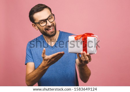 Wonderful gift! Adorable photo of attractive man with beautiful smile holding his birthday present box isolated over pink background.
