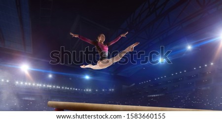 Female gymnast doing a complicated trick on gymnastics balance beam in a professional arena.