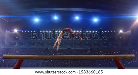Female gymnast doing a complicated trick on gymnastics balance beam in a professional arena. Royalty-Free Stock Photo #1583660185
