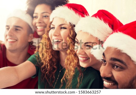 celebration and holidays concept - happy friends in santa hats taking selfie at christmas party