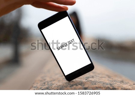A hand holds a mobile phone with the camera turned on. Behind the phone the image of a girl