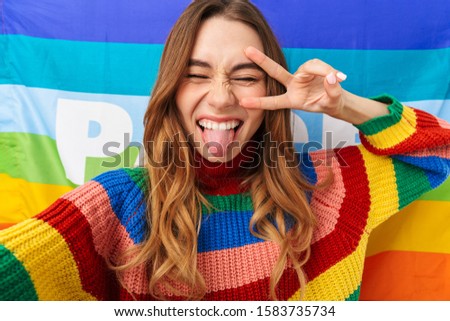 Happy young girl wearing colorful sweater standing over colorful flag background, lgbt concept, celebrating, taking a selfie