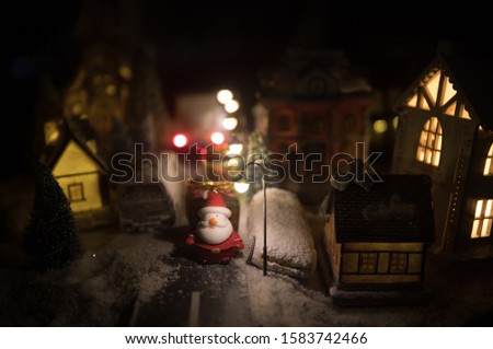 Little decorative cute small houses in snow at night in winter, Christmas and New Year miniature house in the snow at night with fir tree. Holiday concept. Selective focus