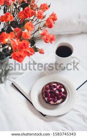 Fruit cake with cup of black tea staying on open book with orange roses in bed closeup. Good morning. 