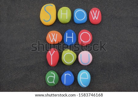 Show who you are, motivational phrase composed with multi colored stone letters over black volcanic sand