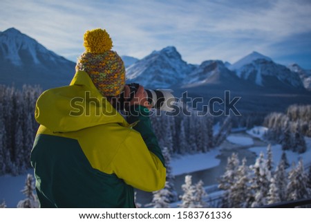 A Man is photographing beautiful snowy mountain scenery. Man in winter clothes and telephoto lens taking pictures of a beautiful mountain landscape. Picture from side and back.