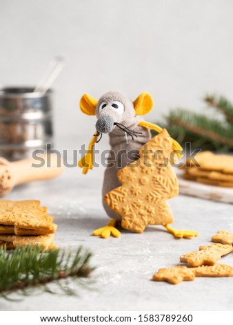 Funny and cute toy rat (symbol of 2020) with yellow ears stealing gingerbread cookie in the shape of christmas tree, can be used as a christmas  and new year card, winter background.
