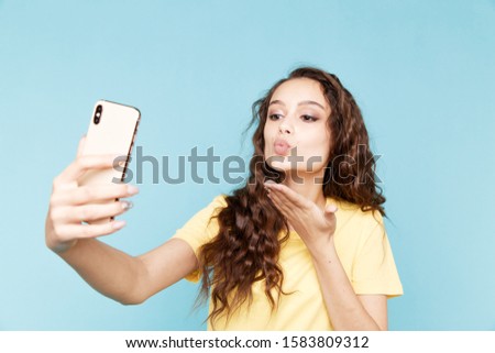 Young woman making self photo and kiss in the blue studio.