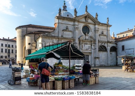 A vendor's vegetables' kiosk at a square in Venice, Italy. A Christian Catholic church in the background.  