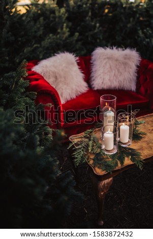 Christmas styled wooden table with candles and tree branches. Red velvet couch in the background. Concept of design and winter decorations.