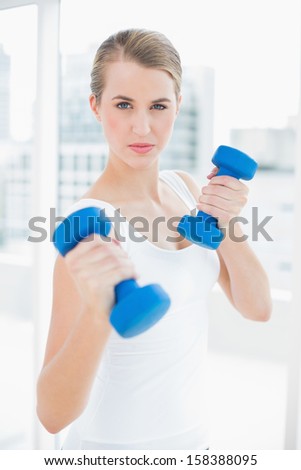 Sporty pretty woman exercising with dumbbells in bright sports hall