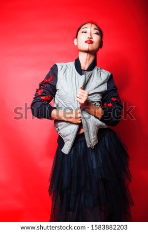 young pretty asian girl posing cheerful on red background, fashion makeup and clothers