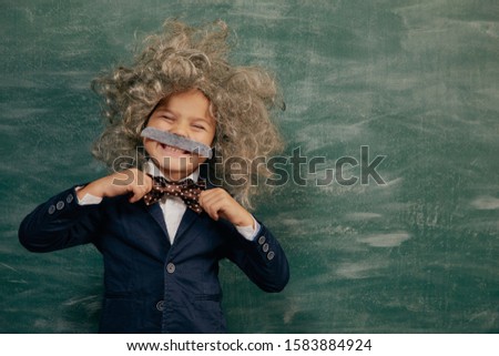 Cheerful smiling little kid (boy) against green chalkboard. Looking at camera.  School concept