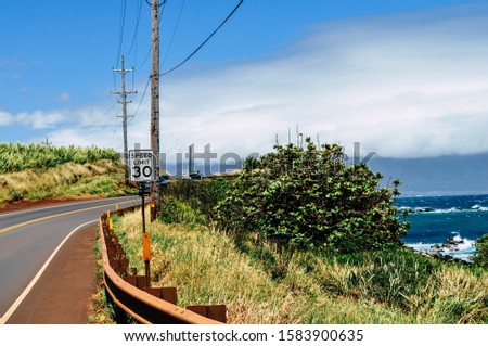 30 MPH speed limit sign posted on a coastal road by the blue ocean on a warm colorful summer day with power lines and guard rails lining the road from the cliff drop.
