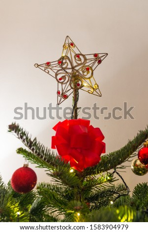 Christmas star on a decorated pine tree with a big red knot under it. Beautiful vertical close shot.  Winter holidays, December. 
