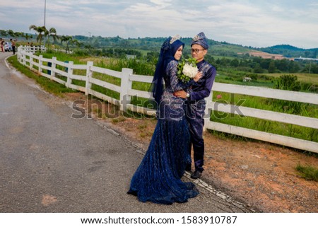 Outdoor shooting for happy Malay wedding couple .The brides and grooms wearing navy blue  Malay traditional cloth with beautiful  scenery as  background. Happiness Concept