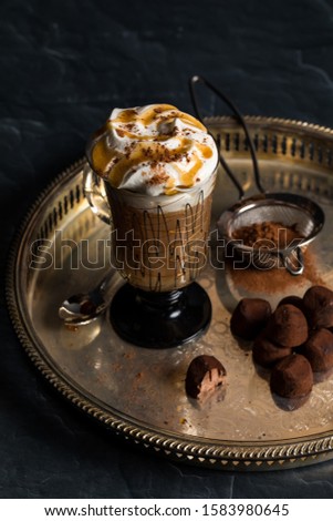 A close up of a hot beverage with whip cream, crushed pecans and cocoa sprinkled on top and served with chocolate truffles.