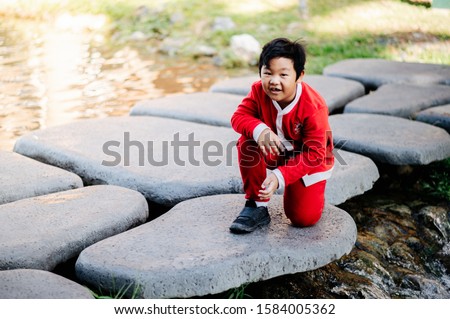 The boy in the Santa outfit is smiling and laughing happily. Sitting on a rock