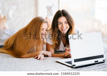 Best friends watching funny video or comedy movie and laughing. Two females with laptop. People, friendship and leisure concept