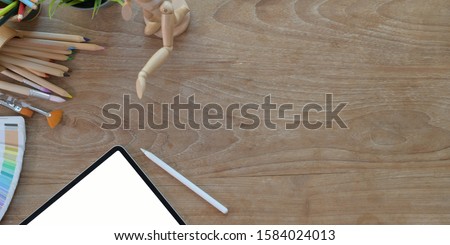 Top view of comfortable artist workplace with painting tools and tablet on wooden table 