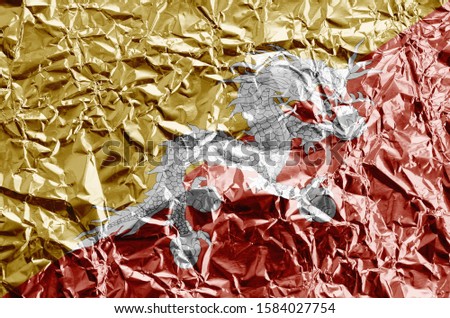 Bhutan flag depicted in paint colors on shiny crumpled aluminium foil closeup. Textured banner on rough background