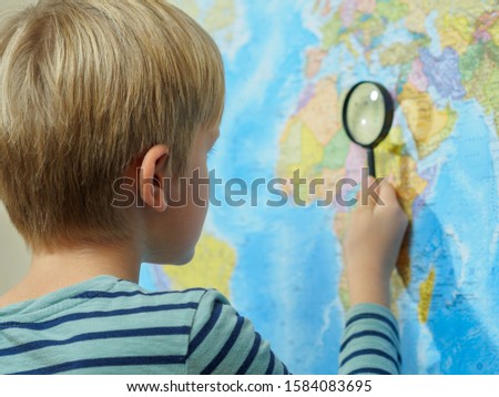 The boy looks at the map through a magnifying glass.