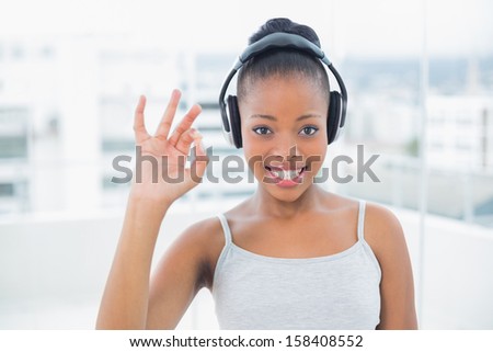 Smiling woman listening to music with headphones and showing okay sign while looking at camera