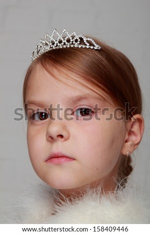 Studio image of a lovely young girl with a tiara and white fluffy cape on gray background on Beauty and Fashion