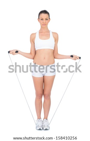 Serious woman in sportswear exercising with skipping rope on white background