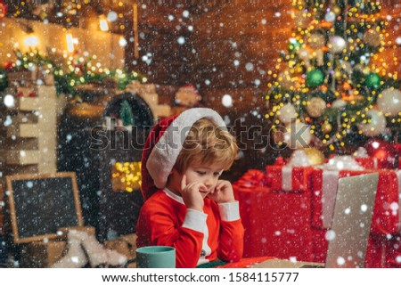 Buy christmas gifts online. Christmas shopping concept. Gifts service. Santa little helper. Smart toddler surfing internet. Little boy santa hat and costume. Boy child with laptop near christmas tree.