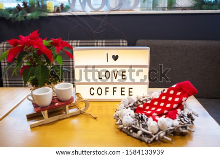 Banner I love coffee stands on a wooden table with red mittens and cups of coffee.