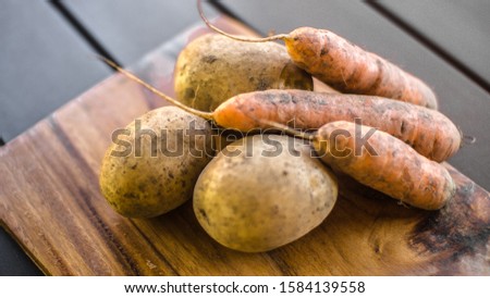 Potatoes and carrots on wooden the board on brown table background