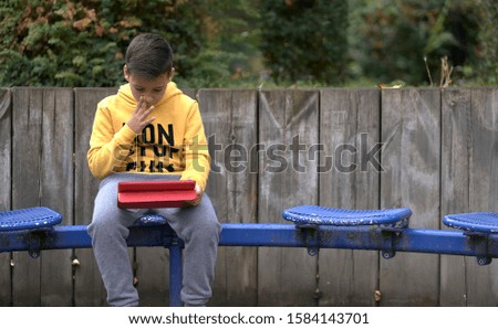 Boy with yellow sweatshirt surfing with his tablet in the street