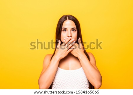 the girl covered her mouth with both hands, the woman shocked on a yellow background, the concept of silence