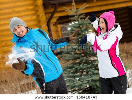 Cute couple having fun outdoors during winter vacations and playing at snowballs