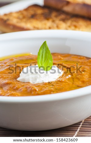 A picture of a white bowl full of fresh tomatoes soup with basil leaves on top 