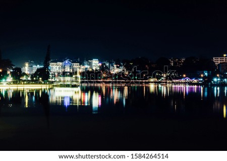 Beautiful long exposure landscape picture of Xuan Huong lake, Da Lat, Vietnam at night. Neon lights of the buildings and their reflections create mesmerizing color trails on the water surface