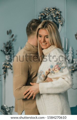 Happy stylish family couple surprising each other with christmas presents. Husband closing eyes of his excited wife. cozy moments in winter holidays at decorated tree. seasonal greetings concept.
