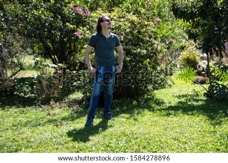 A blond and caucasian man posing for photos and enjoying the sun and nature in spring afternoon in the Brazilian countryside. Photographic model in outdoor and rural photo shoot.