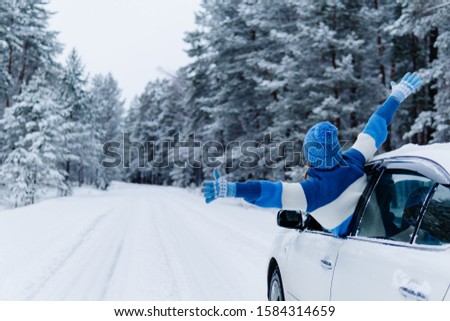 Rear view of adult woman in car over snowy forest on winter roadtrip. Wanderlust concept. Winter travelling scene.