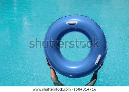 Hands holding rubber blue swimming ring above the water in swimming pool. Swimming concept.