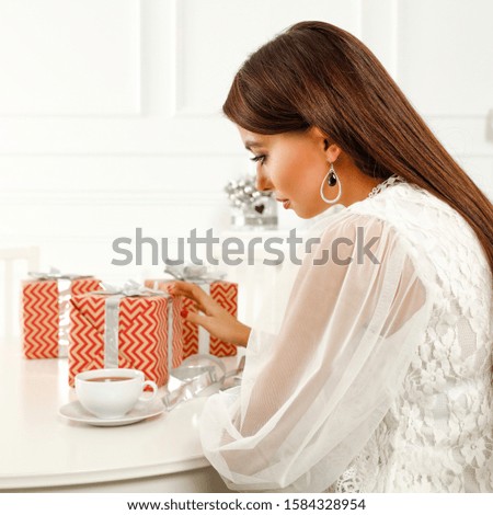 Woman in home interior packing gifts.Free space for your decoration on wooden white table.White home interior and sun light from window.Copy space. 
