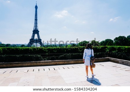 Blue dressed caucasian female model in front Eiffel tower at Square du Trocadéro. Blue and cloudy background at mid-day