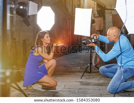 Professional photo shooting outdoors. Attractive glad pleasant beautiful positive female model posing to photographer on city street
