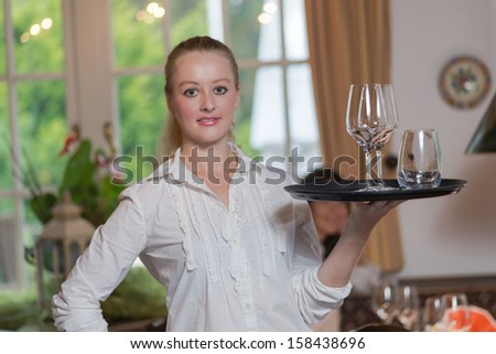 Young blond waitress in restaurant holding a tray full of glasses