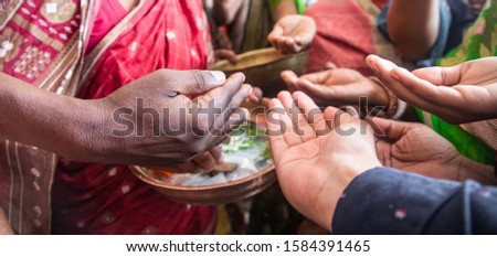religious Indian woman gives a sacred sweet drink called charinamrita after a religious ceremony called Puja.