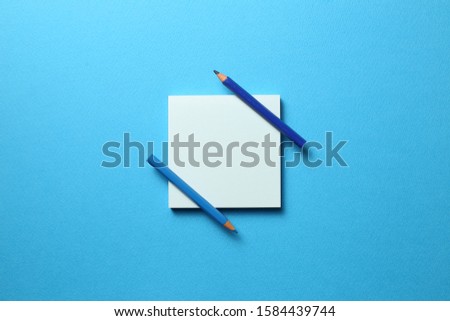 Blue memo note pad and blue colored pencil on blue background