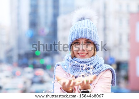 Beautiful young woman holding garlands of lights in her hands. Yellow bokeh. Outdoor portrait. Christmas Holidays